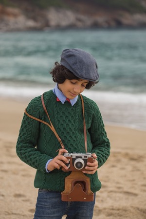 Teenager wearing flat cap and green sweater, holding vintage film camera in his hands. Vertical composition.の写真素材
