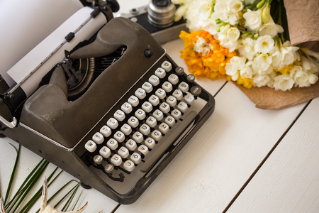 Freelance and writing concept. Retro typewriter on white wooden tabletop with flowers and vintage camera blurred.の写真素材