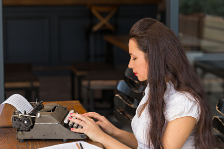 Freelance and writing concept. Sideview potrait of a female writer working in dark interior using a retro typewriter with paper. Copy space.の写真素材
