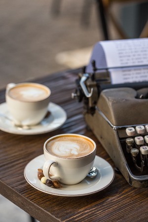 Two cups of cappuccino on a wooden tabletop with retro typewriter.の写真素材