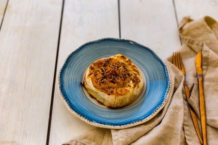 Turkish pastry borek in blue creamic plate on white wooden tabletop. Copy space.