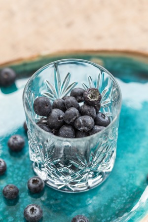 Healthy eating. Blueberries in crystall glass placed on turquoise ceramic plate. Vertical...