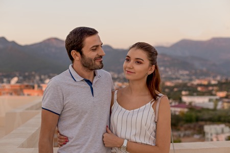 Portrait of a young couple in summer outfit, smiling and posing in front of mountain and cityview.の写真素材