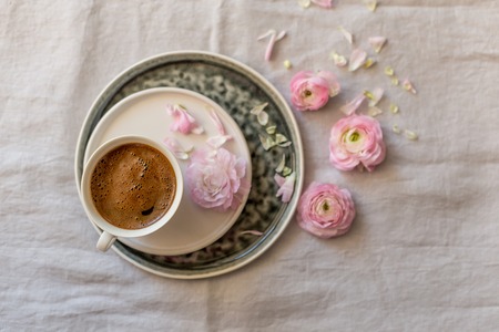 Upper view shot of a cup of coffee in the middle of floral frame of pink ranunculusの写真素材