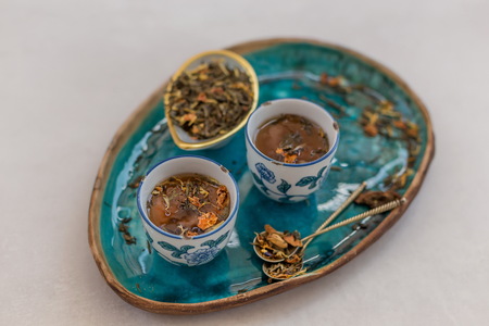 Horizontal shot of herbal tea in white and blue Asian style ceramic cups located in turquoise ceramic tray over light gray tabletop.の写真素材