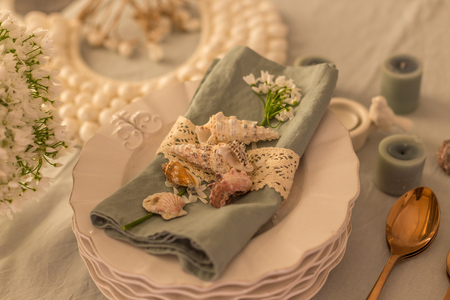 table setting with white rustic tableware, flatware in copper color, washed cotton linen, candles and white spring flowers. Horizontal composition.の写真素材