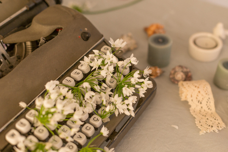 Horizontal shot of a vintage typewriter with white spring flowers placed between it's keys.の写真素材