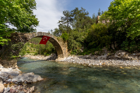 Old stone bridge over the mountain river with crystal clear water and the flag of Turkey hanging from that bridgeの写真素材