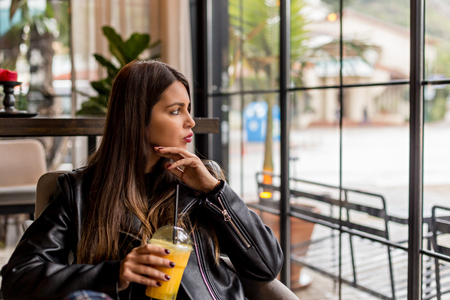 Female in a cafe holding a glass of orange juice and looking through the windowの写真素材