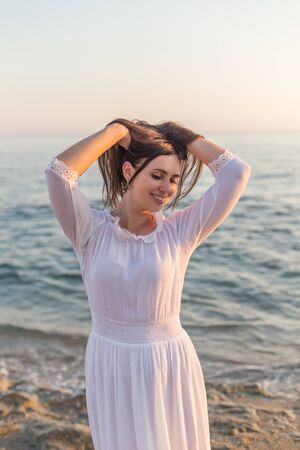 Vertical portrait of a beautiful young brunette female posing at sunset light in front of the seaの写真素材
