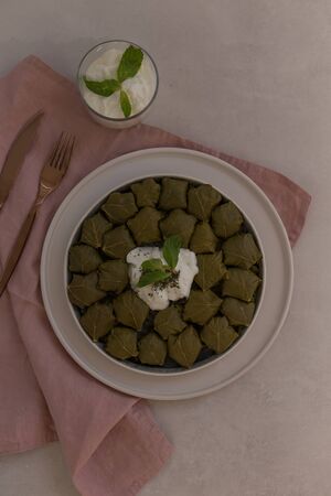 staffed grape leaves (dolma) in a ceramic plate laying on light gray tabletop and pink linen napkin, accompanied with elegant copper color cutlery. Copy space.の写真素材