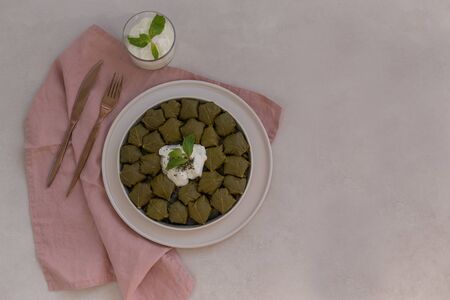 staffed grape leaves dolma in a ceramic plate laying on light gray tabletop and pink linen napkin, accompanied with elegant copper color cutlery. Copy space.の写真素材