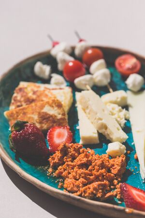 Mediterranean cheese platter with variety of cheese, strawberries and cherry tomatoes served on a turquoise ceramic plate.の写真素材