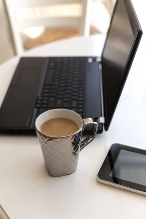 Home office mockup. A table with a cup of coffee, black laptop and tablet.の写真素材