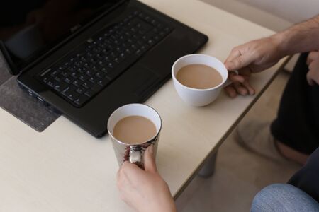 Home office mockup. Black laptop and hands holding cups with cof