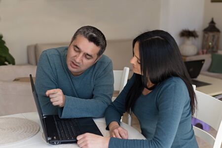 Couple in matching outfites working from home using black laptopの写真素材