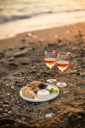 Vertical image of the  romantic beach picnic for two at sunset with two glasses of rose wine, croissants, camamber cheese and figs. Negative space.の写真素材
