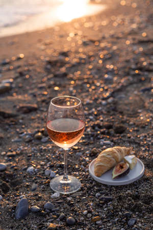 A glass of rose wine on the beach served with croissants and figs. Negative space. Shallow depth of field.の写真素材