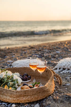 Vertical image of the beach picnic with wine, figs, croissants and camamber cheese in a woven basket. Negative space.の写真素材