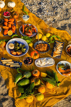 Beach picnic with the a great variety of Mediterranean dishes, vegetables, pastry, cheese, olives and autumn fruits over yellow woven blanketの写真素材