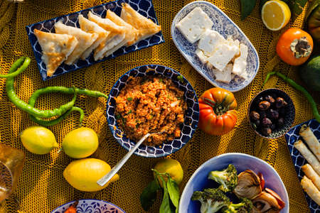 Topview image of bulgur, pastry, whitÑ cheese, olives, grilled brokkoli and onions in ceramic plates with blue and white pattern placed on a yellow woven blanketの写真素材