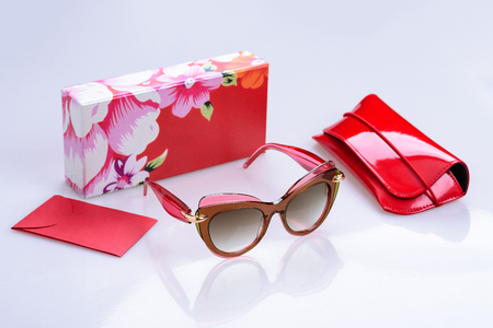 Sunglasses in a modern fashionable frame, box, pouch and envelope on a white glossy background with reflectionの写真素材