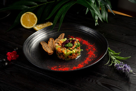 salmon tar-tar on a black plate on a wooden backgroundの写真素材