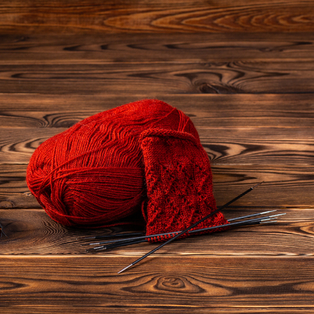 Red ball of yarn and knitting needles with knitting on wooden backgroundの写真素材