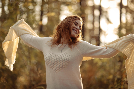 red-haired girl in bright clothes on a background of autumn forest on a sunny dayの写真素材