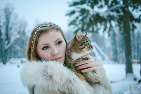 beautiful girl in a beige short fur coat with flowing hair holding a tabby color catの写真素材