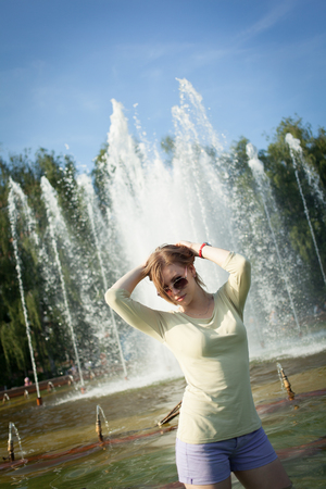 beautiful girl with flowing hair in short shorts and sunglasses is standing in the fountainの写真素材