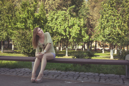 beautiful girl with flowing hair in short shorts and shoes with heels sitting on a benchの写真素材