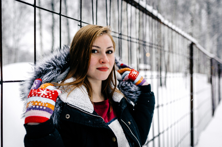 the beautiful girl beside the fence of metal bars amid winter forestの写真素材