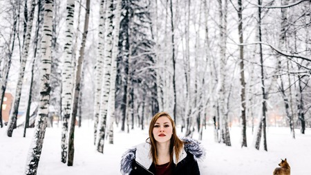 close-up portrait of a beautiful girl in the black jacket with fur hood amid winter forestの写真素材