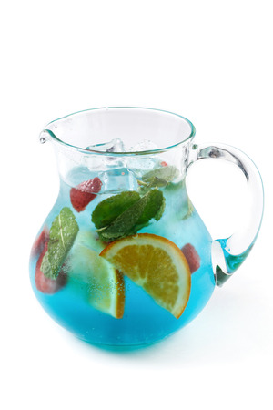 blue fruit lemonade with mint, slises of strawberry and oranges in a glass jug on an isolated white backgroundの写真素材