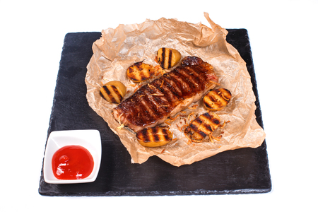 fried steak with potatoes on baking paper and tomato sauce in a cup on a black board on an isolated white backgroundの写真素材