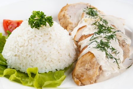 baked chicken in white pot and rice on a sheet of greens in a white plate on an isolated white background closeupの写真素材