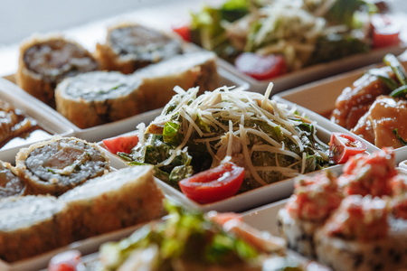 Assorted Japanese dishes in white square plates on wooden stands on the background of a wooden table with gray napkinsの写真素材
