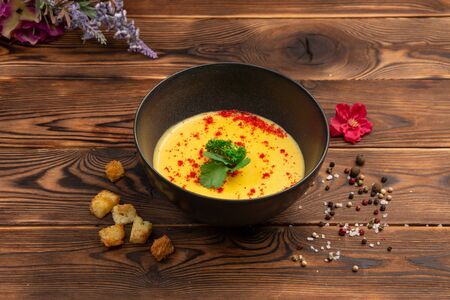 delicate cream soup of red lentils with cream-based vegetables in a black plate on a wooden backgroundの写真素材