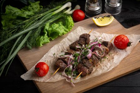 beef kebab with pickled onions and cilantro on a wooden board decorated with leafy greens on a dark backgroundの写真素材