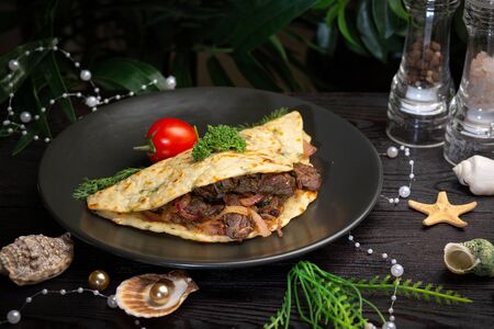 Chinese onion tortilla with beef and onions in a black plate on a dark wooden backgroundの写真素材