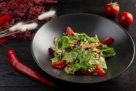 salad with tomatoes and leafy greens in a black plate on a dark wooden backgroundの写真素材