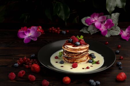 pancakes with condensed milk decorated with berries in a black plate on a dark wooden backgroundの写真素材
