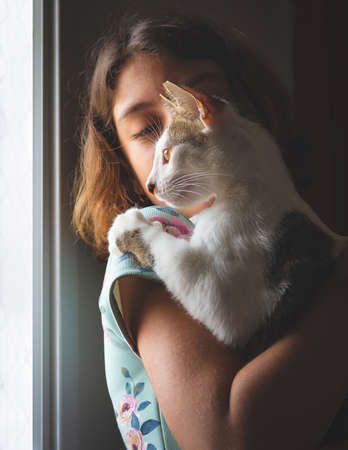 Portrait of an alley cat being held by a little girl, in front of the light coming from a window....