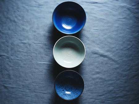 Three decorative bowls in varying shades of blue and white are vertically aligned on a textured bluish grey fabric The composition offers a clean minimalist aesthetic The bowls showcase a depth of color and design that enhances the visual appeal of the settingの素材