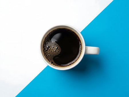Overhead shot of a white mug filled with freshly brewed coffee sitting on a diagonally split blue and white background The coffee has a rich dark color with some visible bubbles on its surface indicating its warmth and freshness The stark contrast between the coffee mug and the colored background draws the viewers eye and makes the image suitable for commercial or advertising useの素材