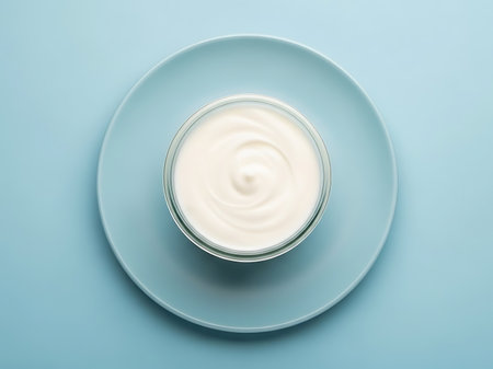 Overhead shot of a clear glass bowl filled with smooth white yogurt set on a simple blue plate The image emphasizes the creamy texture of the yogurt against the cool clean backdrop evoking a sense of health simplicity and mindful eating The minimalist aesthetic highlights the purity of the ingredientsの素材