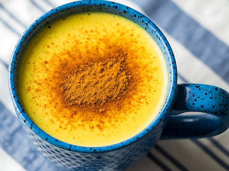 A vibrant turmeric latte is displayed in a speckled blue ceramic mug The creamy yellow beverage is topped with a generous sprinkling of turmeric powder The mug is placed on a surface covered with a blue and white striped cloth adding a touch of pattern and color to the scene The shot captures the drink from an overhead angle highlighting its inviting appearanceの素材
