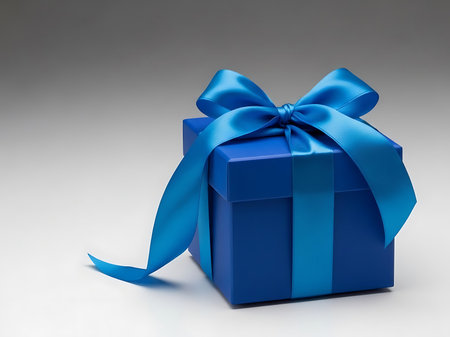 A beautifully wrapped blue gift box with a shiny blue ribbon tied in a bow The box is sitting on a light background and is ready to bring joyの素材
