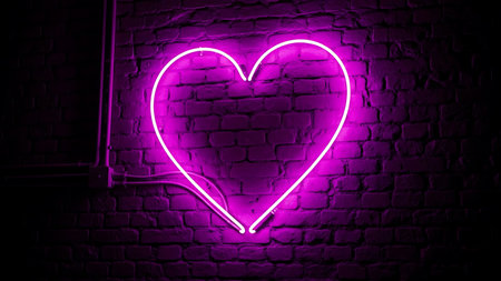 A glowing neon heart sign emits a soft purple light against a rustic brick wall creating a romantic and modern ambianceの素材